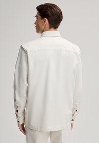 Witte katoenen overhemd met een kraag, lange mouwen en twee knopen op elke manchette. Ontworpen met een relaxed fit en een gladde textuur.