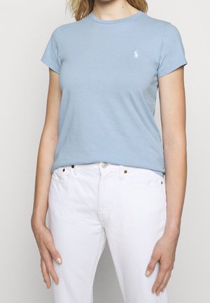 Jasnoniebieska bawełniana koszulka z okrągłym dekoltem, krótkie rękawy, z małym białym haftowanym logo na piersi, zestawiona z białymi spodniami.