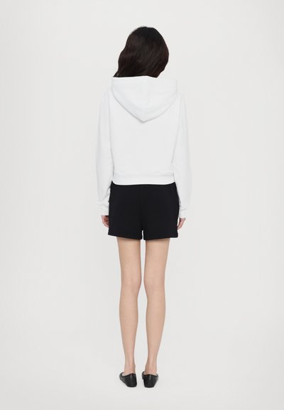 White cropped hoodie with a hood, paired with black shorts. Simple design, soft fabric, and fitted silhouette. Footwear is black flats.