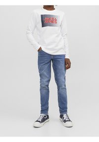 White long-sleeve t-shirt with navy and red graphic print, paired with fitted blue denim jeans and navy sneakers with white accents.