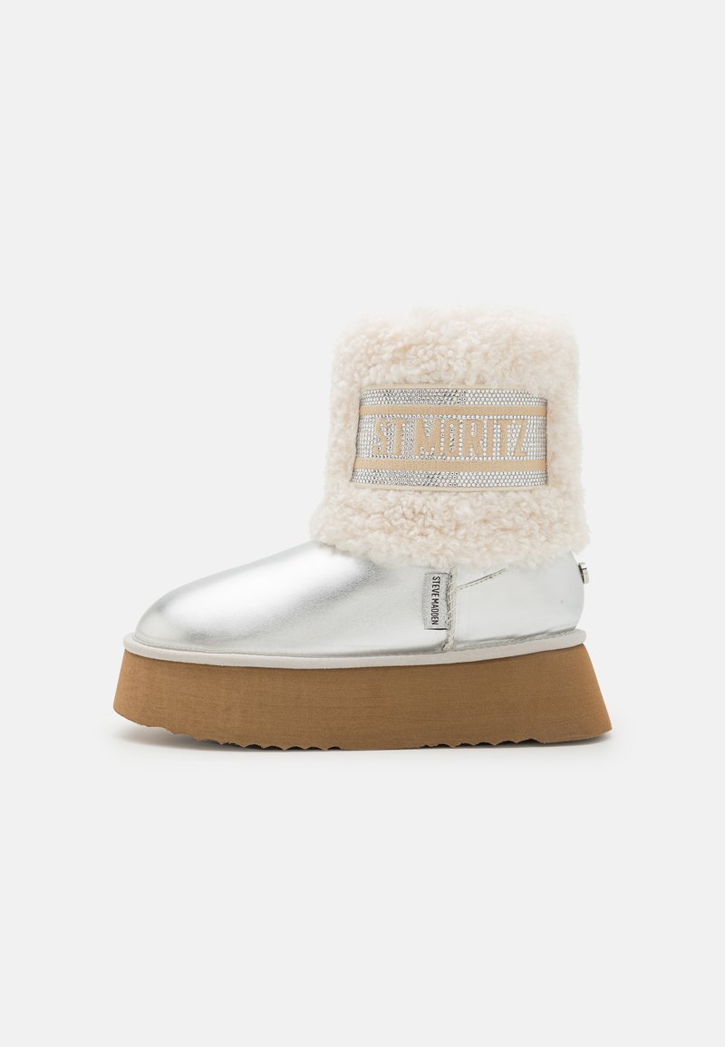 Silver metallic ankle boot with a fluffy cream faux fur collar and a textured brown platform sole. Features a decorative logo band on the collar.