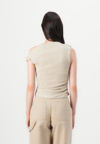 Beige ruched tops ar ar vienu plecu, ar teksturētu audumu. Apvienots ar beigiem platām biksēm ar aizmugurējām kabatām.