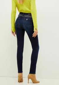 Mörkblå skinny jeans med en prydlig midja, som är kombinerade med en ljusgrön texturerad tröja och nude högklackade ankelstövlar.