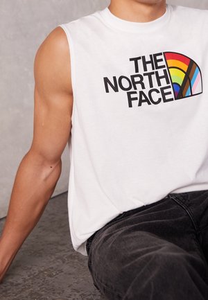 White short-sleeve shirt featuring a colorful semi-circle logo with "THE NORTH FACE" text, paired with dark gray pants. Smooth texture.
