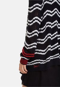 Maglione nero a maglia con righe zigzag bianche e un accento rosso sul polsino, caratterizzato da un tessuto testurizzato e un dettaglio del logo ricamato.