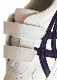 Zapatilla blanca de cuero con detalles en púrpura. Cuenta con correas de velcro y un acabado texturizado. Punta redondeada y forro de malla para una mejor transpirabilidad.