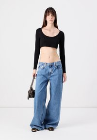 Musta pitkähihaisen crop-top, korkeavyötäröiset vaaleansiniset leveälahkeiset farkut, musta käsilaukku ja eläinkuosilla varustetut kengät yksinkertaisella taustalla.