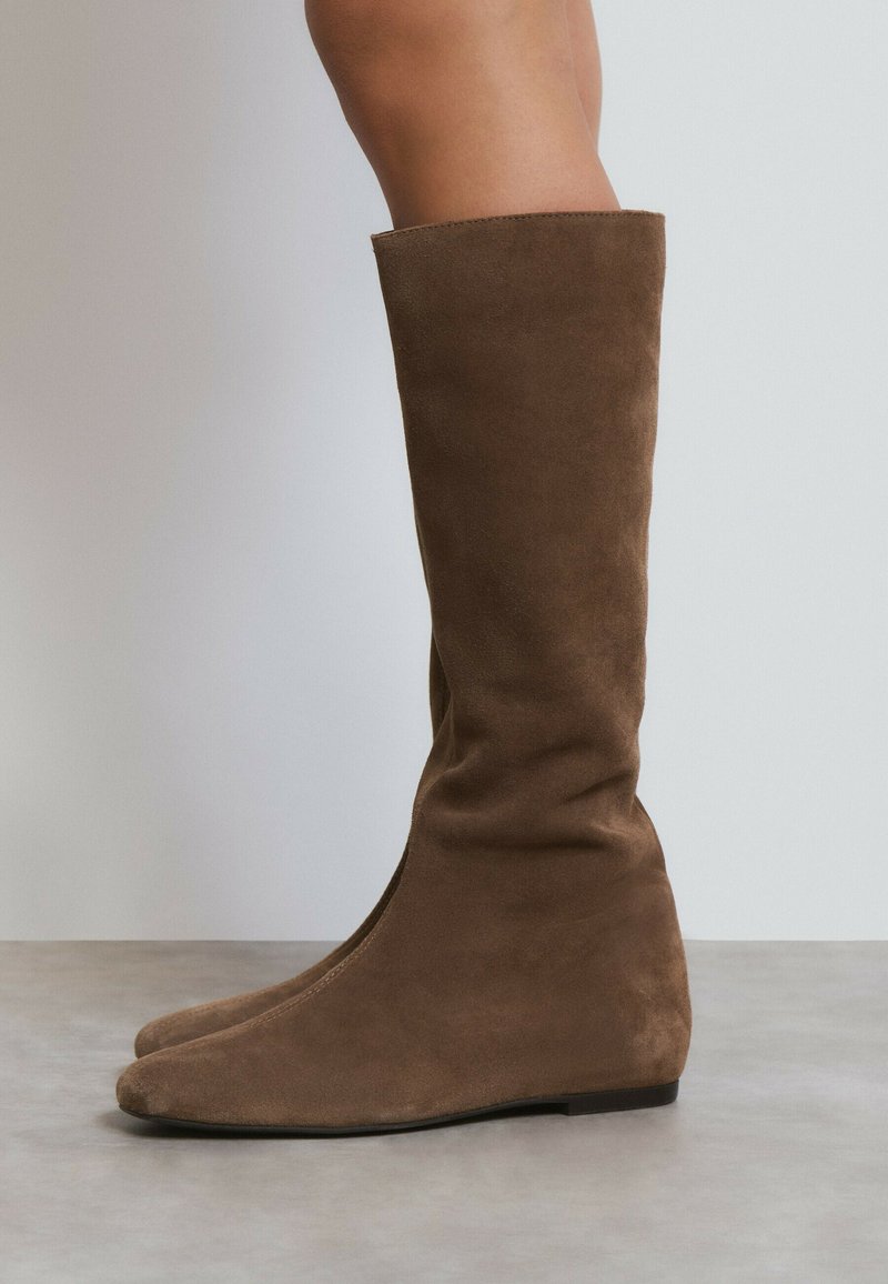 Botas marrones de ante hasta la rodilla con punta afilada y tacón de cuña, con una textura suave y un diseño minimalista.