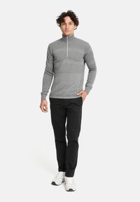 Grauer Pullover mit langen Ärmeln, hohem Kragen und teilweisem Reißverschluss, ausgestattet mit strukturiertem Design und taillierten Ärmeln, kombiniert mit schwarzen Hosen und Sneakers.