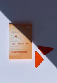 Orange förpackning för "Facial Patches Mini Niacinamide" med 24 bitar visade; plåstren är triangulära och ljusorangea med en strukturerad yta.