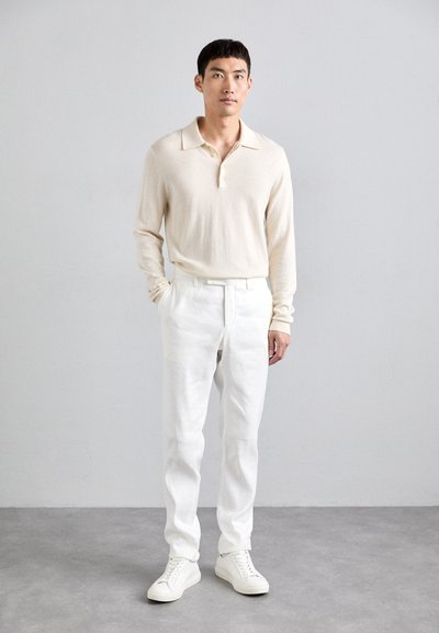 Beige langærmet polo skjorte med krave, parret med hvide linnedbukser og hvide sneakers. Simple, rene linjer og lyse farver.