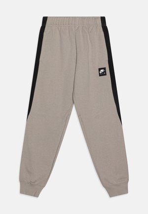 Pantalones de chándal gris claro con paneles laterales negros. Cintura elástica, puños acanalados y un pequeño parche con el logo de Nike en el frente. Tejido suave y texturizado.