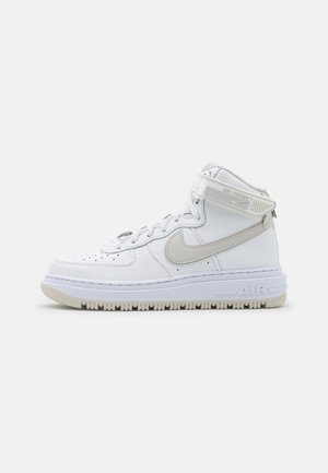 Højt hvidt sneakers med lysegrå Nike swoosh, ankelrem, perforeret tå og tyk sål med "AIR" mærkning på siden.
