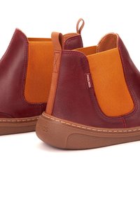Botas de tobillo de cuero rojo con paneles elásticos naranjas, suela marrón claro y tira en la parte trasera. Detalles de costura en la parte superior.