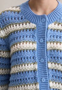 Dzianinowy kardigan w kolorze niebieskim z białymi i zielonymi paskami. Posiada ściągaczowy kołnierz oraz sześć jasnoniebieskich guzików. Teksturalny, ażurowy wzór.