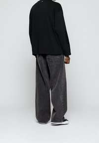 Musta pitkähihaispaita ja harmaat väljät farkut. Paidassa on rento istuvuus ja hihassa logo; housut on valmistettu teksturoidusta kankaasta.