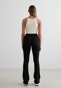 Canotta bianca aderente abbinata a leggings neri a campana, realizzati in un tessuto morbido, che mettono in risalto un design semplice e una silhouette sagomata.
