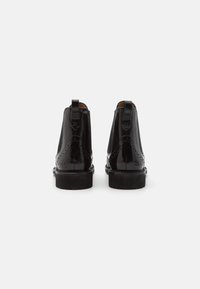 Bottes chelsea en cuir verni noire avec détails brogue, finition lisse, anses de tirage et un petit talon empilé.