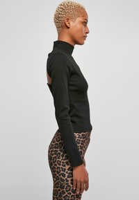 Svart langermet topp med høy krage og utskjæring detalj på baksiden, kombinert med tettsittende leopardmønstrede leggings.