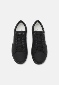 Černé tenisky vyrobené z umělého materiálu s šněrovacím designem, hladkým povrchem, kulatou špičkou a jemnými šedými akcenty na stranách.