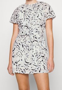 Kortärmad klänning i lätt tyg, med ett ljusblått och svart vågigt mönster, med en rynkad halsringning och knytbälte i midjan.