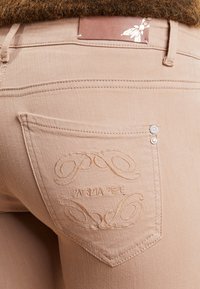 Beiga denimjeans med broderad bakficka som har "Patrizia Pepe"-logotypen och dekorativa virvelmönster. Inkluderar detalj med metallknapp.