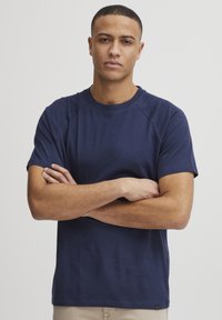 Temno modra kratka majica s kratkimi rokavi iz mehkega materiala, z okroglim izrezom in raglan rokavi. Vključuje majhen logo na robu.