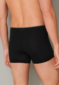 Černé bavlněné boxerky s přiléhavým designem, které mají kontrastní elastický pás a hladkou texturu. Zadní pohled ukazuje délku nohou.