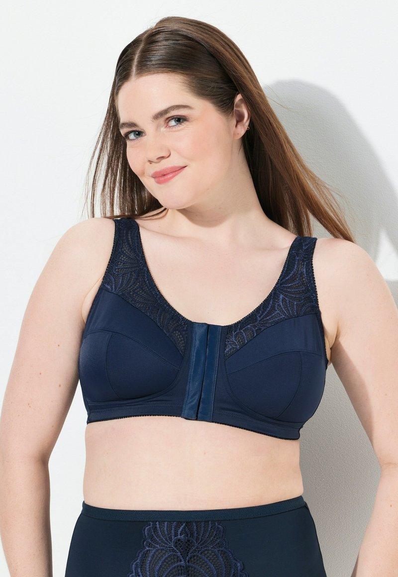 Merinen rintaliivit, jotka on varustettu pitsireunalla, leveillä olkaimilla ja edessä olevan kiinnityksen avulla. Materiaali on sileä, ja rinnan kohdalla on teksturoitu yksityiskohta.