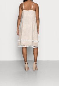 Valkoinen beige ilman hihoja oleva mekko, jossa on timanttikuvio, kerrostettu malli ja valkoiset tupsut helmassa. Yksinkertaiset säädettävät olkaimet.