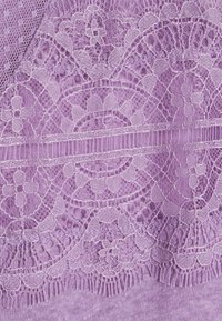 Tissu en dentelle lavande avec des motifs floraux et géométriques complexes sur un fond uni en tricot lavande.