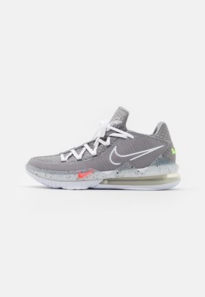 Baskets Nike grises avec lacets blancs, logos swoosh blancs et rouges, semelle intermédiaire mouchetée et semelle à coussin d'air visible sur fond blanc.