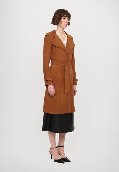 Cappotto trench in suede marrone con vita cintrata, ampi revers e chiusura a bottoni. Presenta polsini decorativi ed è abbinato a una gonna di satin nera.