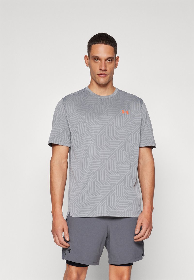Grå kortermet treningsskjorte med geometrisk mønster, med en oransje logo på brystet. Brukt sammen med grå shorts.