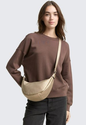 Borsa a tracolla dorata, testurizzata, con forma curva e manico; indossata con una felpa marrone e jeans neri. Design semplice, pochi dettagli.