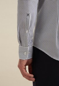 Witte shirt met een blauw rond patroon, met knoopmanchetten en een getailleerde pasvorm. De stof lijkt glad met een subtiele glans.