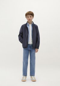 Marine bomberjack over een lichtblauw overhemd, wit shirt en blauwe spijkerbroek. Grijze sneakers met witte accenten. Eenvoudig, casual ontwerp.