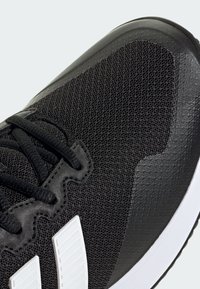 Czarny but sportowy z teksturowaną meshową cholewką, syntetycznymi akcentami, białymi paskami i czarnymi sznurówkami, z białą podeszwą.