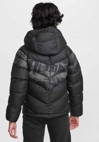 Giacca a vento nera con design a chevron, dotata di cappuccio e una combinazione di texture lisce e decorative sulla schiena.