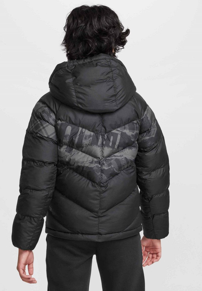 Chaqueta acolchada negra con un diseño en forma de chevron, que incluye una capucha y una mezcla de texturas suaves y con patrón en la parte posterior.