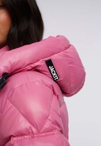 Fuchsia puffjacka med hög krage, med quiltade sektioner och en svart logotags, tillverkad av glänsande, slätt material.