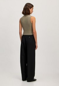 Olijfgroene geribbelde tanktop gecombineerd met hoge zwarte wijde broek. Glad textuur met een minimalistisch ontwerp en geen zichtbare patronen.