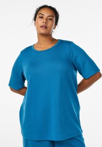 Tyrkysově modrý top s krátkým rukávem z hladké, pružné látky s kulatým výstřihem a volnějším střihem. Bez výrazných vzorů nebo detailů.