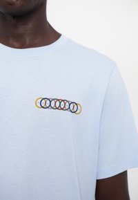 Lyseblå bomulds T-shirt med et multicoloreret cirkellogo og "PAUL SMITH" tekst over brystet. Glat tekstur og rund halsudskæring.