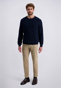 Donkerblauwe textuurtrui gecombineerd met beige broek en donkerbruine leren schoenen. De trui heeft een ronde halslijn en ribbels aan de mouwen.