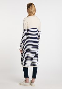 Cardigan lungo a righe crema e blu navy, con maniche lunghe, taglio dritto e spacco laterale. Indossato sopra jeans scuri e sneakers bianche.