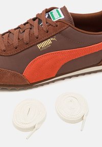 Bruna Puma Arizona-sneakers med en strukturerad ovandel och en orange rand, guld-logotyp och två vita skosnören.