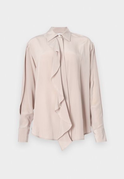 Ljusrosa blus i mjukt tyg, med volang framtill, knäppning vid kragen och lång ärm med manschettdetaljer.