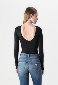 Black long-sleeve bodysuit with low back, adorned with small embellishments. Paired with medium-wash denim jeans featuring a classic cut.