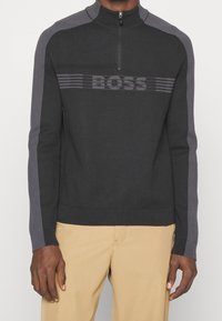 Ciemnoszary sweter dziany z wysokim kołnierzem i półzamkiem. Posiada poziome logo "BOSS" oraz kontrastowe, teksturowane rękawy.